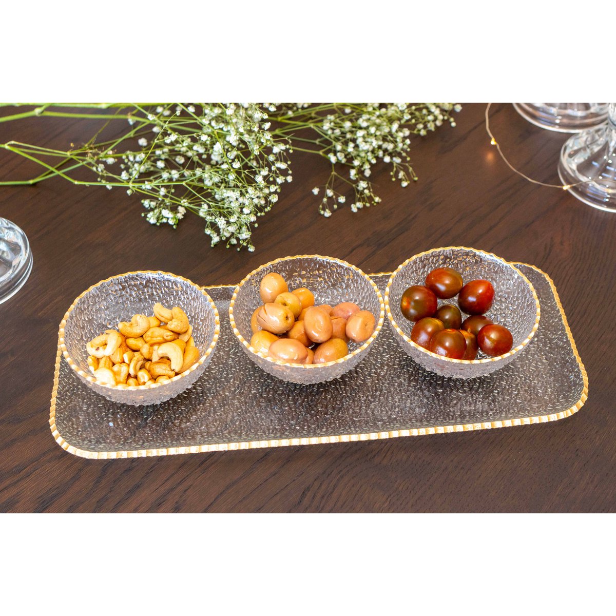 Drei kleine Schalen mit Snacks auf einem dekorativen Tablett auf einem Holztisch