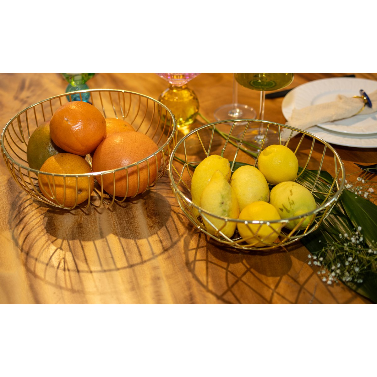 Zwei Drahtkörbe mit Orangen und Zitronen auf einem Holztisch