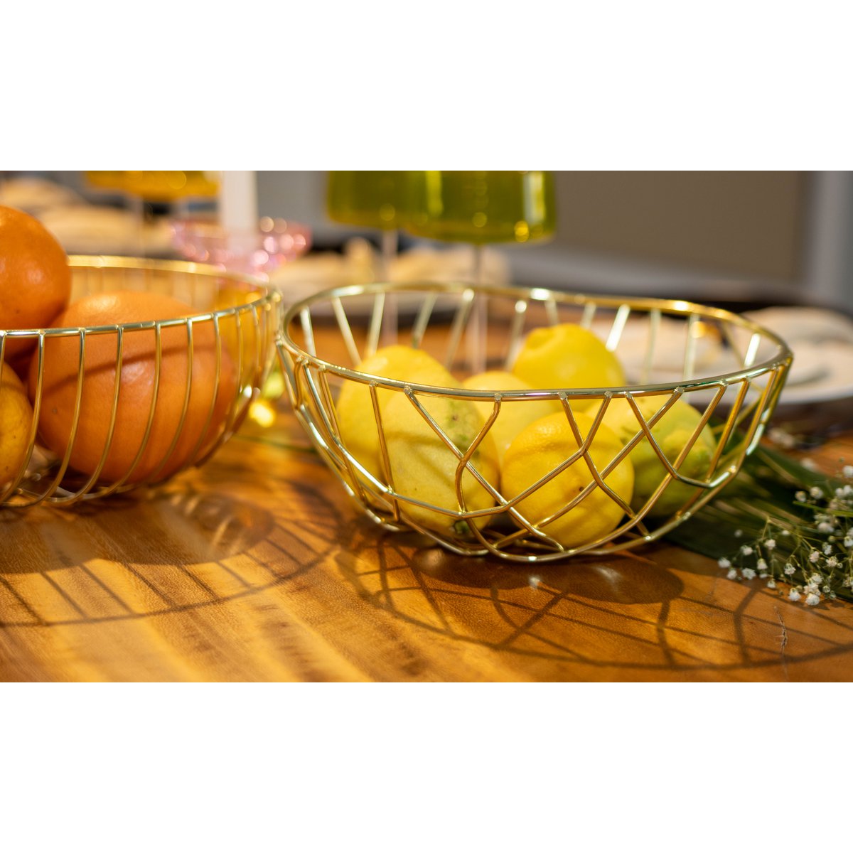 Gold wire fruit bowls with oranges and lemons on a wooden surface