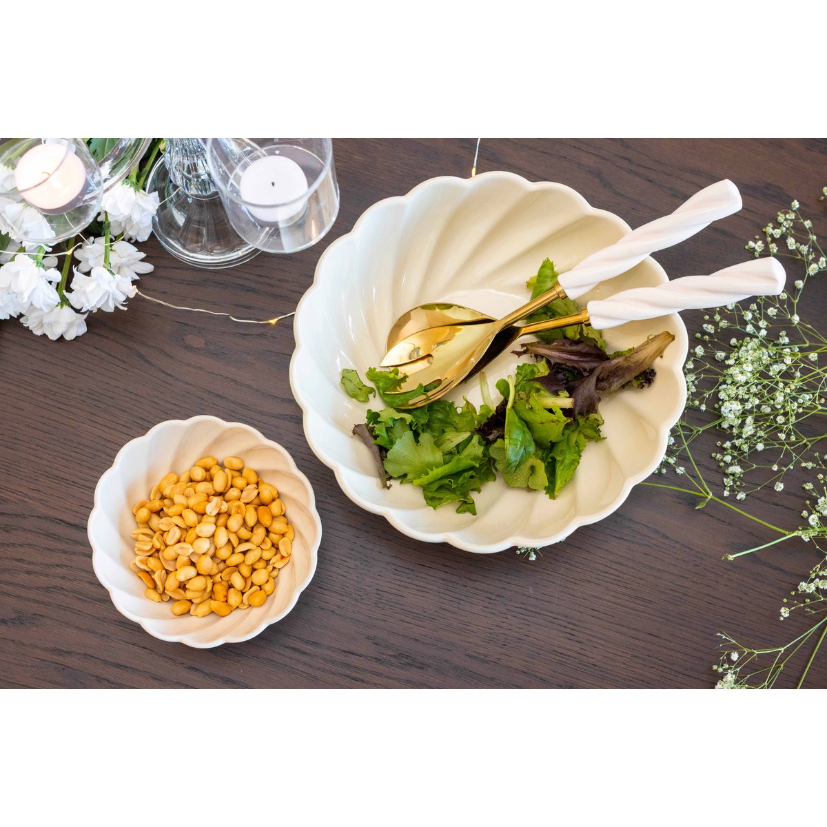 Zwei weiße Schalen auf einem Holztisch, eine mit Salat und eine mit Bohnen, von Blumen umgeben